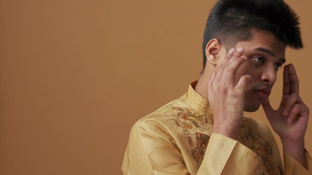 Confident Indian man in national cloth touching his temples in the orange studio