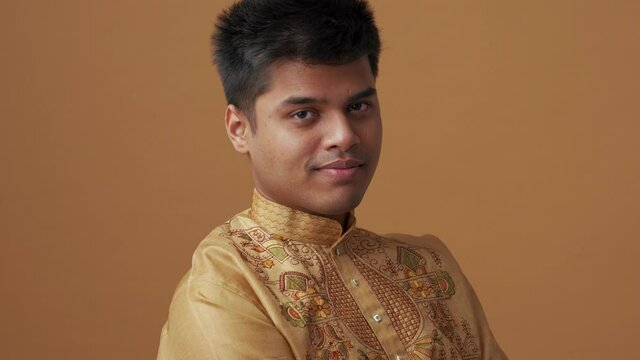 Positive handsome Indian man in national cloth looking at the camera in the orange studio