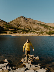 man in the yellow body shirt standing on the stone near mountain lake