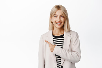 Portrait of smiling corporate girl in beige suit, pointing finger left and looking enthusiastic at...