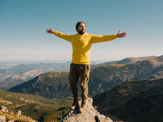 man with beard in yellow body shirt standing at the top of the mountain