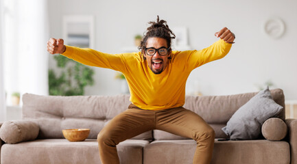 Overjoyed excited young african american man celebrating goal while watching football match on tv - obrazy, fototapety, plakaty