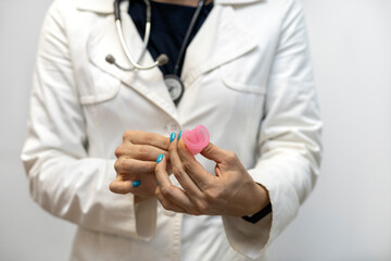 Doctor's hand holds menstrual cup and shows the correct way to insert it. Gynecology and health concept.