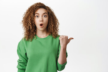 Image of surprised curly woman pointing right, gasping and saying wow, showing store info, logo or banner aside, white background