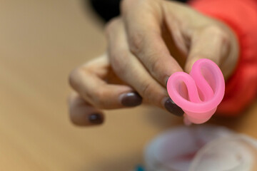 Doctor's hand holds menstrual cup and shows the correct way to insert it. Gynecology and health concept.
