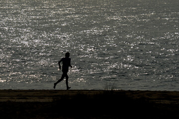 Fototapeta na wymiar 1 Young man jogging on the beach. Athlete silhouetted against the light. Reflections on the sea.