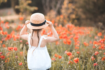Little child girl 3-4 year old wear white dress and straw hat with boy in poppy meadow outdoors....