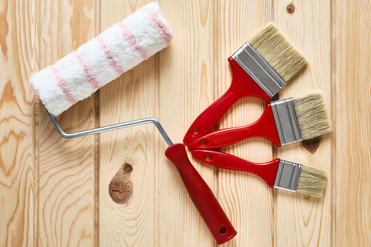 Three red different size paintbrushes and painter roller at wooden surface. Painter tools on wooden background. Top down view