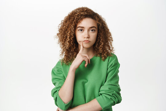 Image of girl with curly hair thinking, posing thouthful, making choice or decision, standing in green sweatshirt over white background