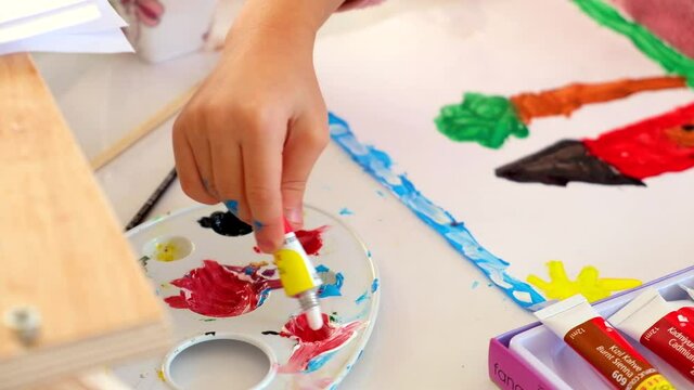 Close-up of children hand putting paint to artist palette. Child paints using acrylic paints set