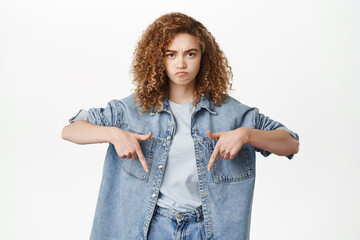 Angry young woman pointing fingers down and looking grumpy, grimacing upset, complaining at store...