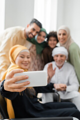 happy asian woman taking selfie with blurred interracial muslim family.