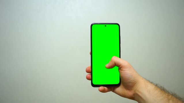 Man using smartphone viewing green screen scrolling on mobile phone browsing chroma key . close up male hands . Mobile phone mock-up