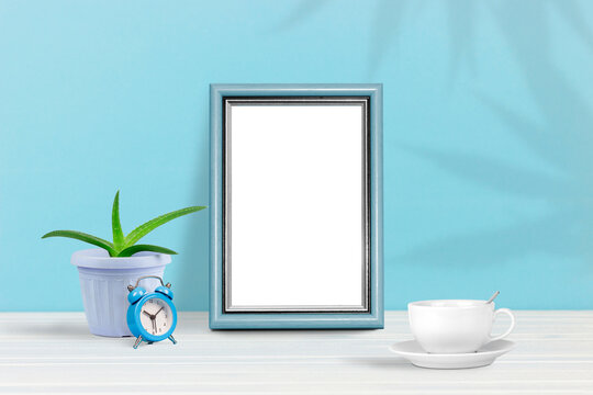 Poster template. Photo frame on wooden table with home flower, alarm clock and coffee cup
