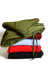 Stack of folded hoodie and hooded sweatshirts on white background. Trendy comfortable casual clothes. Closeup. Vertical orientation.