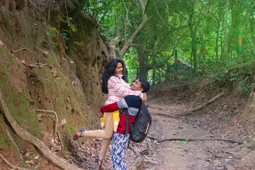 Indian young married woman being carried by her husband in forest. Couple having fun on their summer holiday. Togetherness and happiness concept. Authentic real people, family in outdoor.