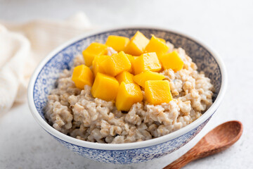 Oatmeal porridge in bowl with mango cut in cubes. Healthy breakfast for weight loss and wellness.