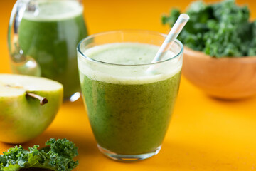 Glass of green vegetable fruit detox smoothie on yellow table background