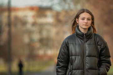 A young beautiful girl in a dark jacket is walking down the street.