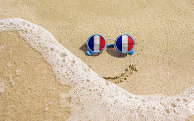 Sunglasses with French flags on a sandy beach. Nearby is a sea lightning and a painted smile. The concept of a successful vacation in the resorts of France.