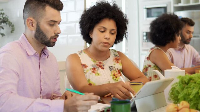 Black Woman Working With Partner And Using Tablet In Kitchen Table.
