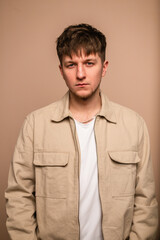 Obraz premium Beautiful young guy model with a fashionable hairstyle in a beige jacket and a white T-shirt in the studio, looking into the camera