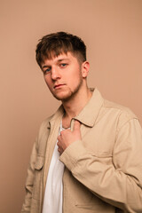 Obraz premium Handsome and attractive young male model with fashionable hairstyle posing for the camera. Man in stylish jacket and white T-shirt on beige background