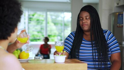 Black woman welcomes friend to toast with healthy drink in small afternoon meeting. Female friends drinking and eating heathy food
