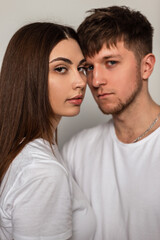 Beautiful young couple in stylish classic white t-shirts in the studio. Pretty woman and a handsome man with a haircut in fashionable clothes in the studio.