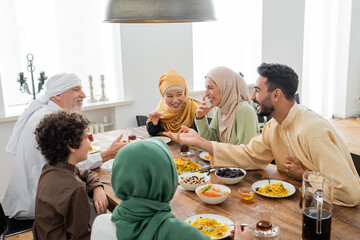 Fototapeta na wymiar young arabian man talking to cheerful multicultural muslim family during dinner.