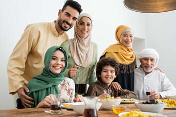 multicultural muslim family smiling at camera near served pilaf and tea.