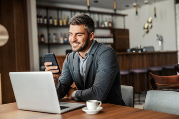 A happy businessman is sitting in a coffee shop and checking on his bank account on the mobile....