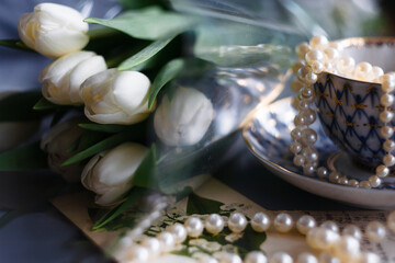 Obraz na płótnie Canvas White tulips in buds on a white background with pearl beads and a cup. Spring composition.