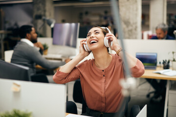 Carefree businesswoman enjoys in music over headphones in the office.