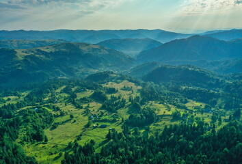 Aerial view of a fog creeping over the mountains surrounding the valley on a summer day in the morning. Aerial drone view of houses in a mountain valley on a summer day.