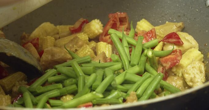Adding Fresh Green Beans Into Delicious Thai Chicken Curry Cooking In A Wok. close up
