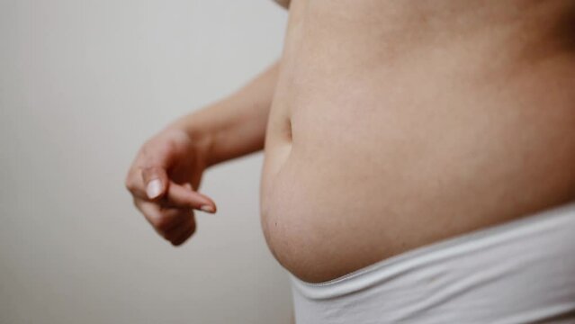 Fat woman using her hands to squeeze out excess fat that is isolated on beige background.