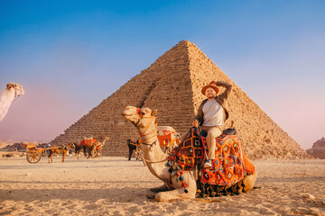 Tourist man with hat riding on camel background pyramid of Egyptian Giza, sunset Cairo, Egypt - Powered by Adobe