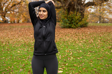 Woman in black sports clothing and hijab stretching in park