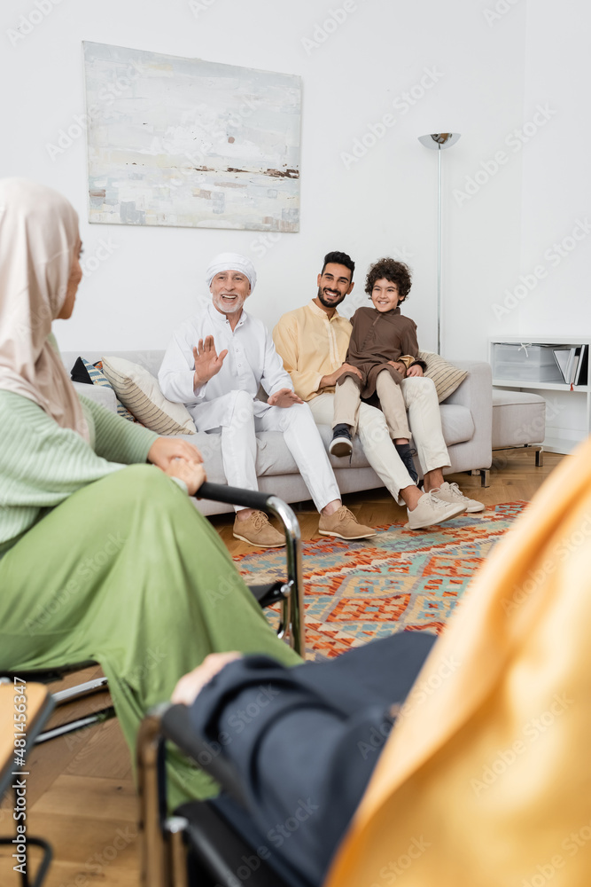 Wall mural mature muslim man waving hand while talking to multicultural family in living room.