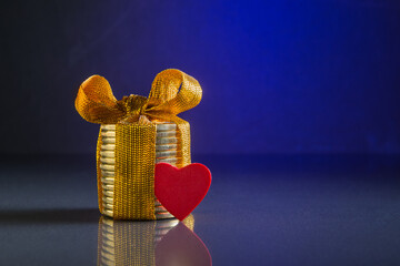 Stack of coins with golden bow and red heart over blue background with copy space. Money and love conceptual idea