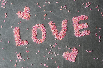 Word Love and Valentines hearts made of small red rocks on grey stone background