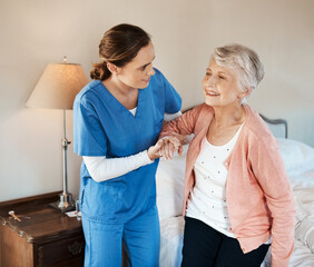 I'm ready for a day out. Shot of a young nurse helping a senior woman get up from her bed in a...