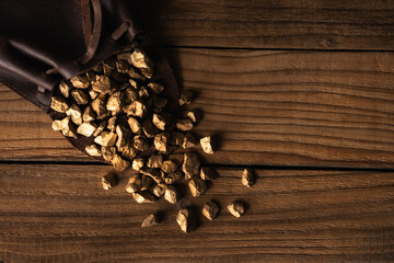 A pouch with scattered gold nugget grains, on wooden background. Pile of gold. Copy space.