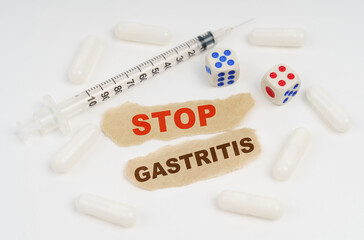 On a white surface lies a syringe, pills, dice and pieces of paper with the inscription - STOP GASTRITIS