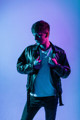 Handsome brutal fashionable young man in stylish outerwear with a fashion leather jacket and white t-shirt in a colored studio with neon pink light.