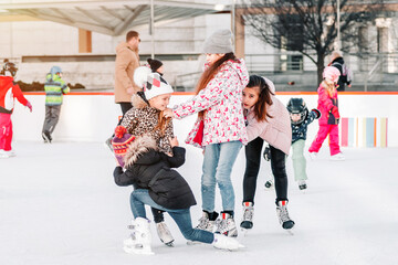 Soft,Selective focus.People, friendship, sport and leisure concept - happy friends on skating rink.Group of teenage friends ice skating on an ice rink.Funny moment fell on the ice skating rink © Nataliia