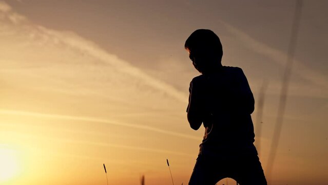 Silhouette of kid in park. Boy is engaged in boxing with shadow in park. Kid boxing. Silhouette of child at sunset in park. Happy boy goes in for sports boxing with shadow. Happy child at sunset