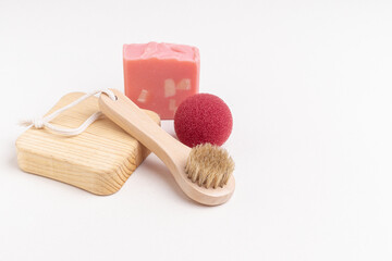 Fototapeta na wymiar Wooden brush for facial or body massage, pink soap and red makeup remover sponge. Space for text