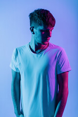 Handsome young man with hairstyle in a white T-shirt in the studio against multi-colored pink neon...
